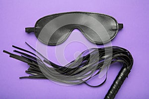 Set of erotic toys for BDSM. The game of sexual slavery with leather blindfold and whip on violet background. Intimate games. Copy