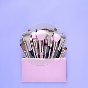 Set of essential professional make-up brushes and cosmetic bag on pastel purple background