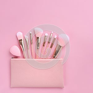 Set of essential professional make-up brushes and cosmetic bag on pink background