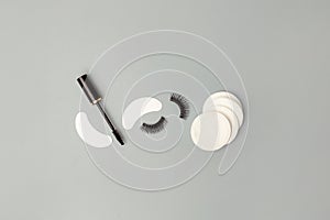 Set for eye lash extension on trendy gray background. Fake eyelashes, mascara brush, cotton pads. Beauty concept, makeup cosmetics