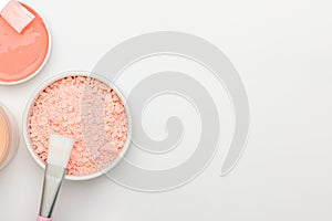 A set of face masks in white open container with brushes close-up on white background. Pink alginate powder and liquid