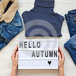 Set of female autumn clothes, female hands holding lightbox with `Hello autumn` words. Overhead view, from above, flat lay