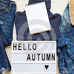 Set of female autumn clothes, lightbox with text `Hello autumn`, blank notepad. Top view, from above, flat lay. Space for text