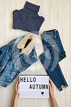 Set of female autumn clothes, women`s hands holding modern board with text `Hello autumn`. Overhead view