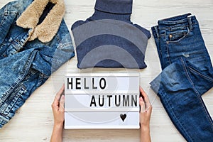 Set of female autumn clothes, women`s hands holding modern board with text `Hello autumn`. Overhead view, from above