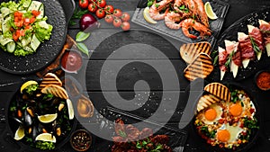 Set of food from meat, fish and salads on black background. Top view.