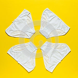 Set of four white women`s panties on a bright yellow background. Flat lay.