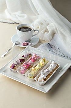 Set of French dessert eclairs with colorfulicing and cup of coffee on the table