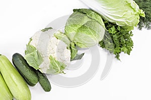 Set of fresh raw organic green vegetables and greens diagonally on a white background.