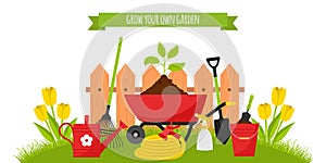 A set of garden tools, a wheelbarrow with seedlings on the background of a lawn with tulips and a fence. Bucket, watering can,