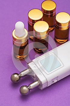 A set of gels in ampoules and a device for microcurrent stimulation of facial muscles on a purple background