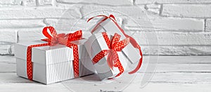 Set of gift boxes with red ribbon on a white wooden table, brick backdrop, banner. Selective focus