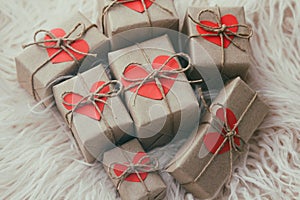 Set of gift boxes wrapped in craft paper and tie hemp string. With cardboard hearts. White fur background.