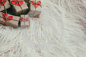 Set of gift boxes wrapped in craft paper and tie hemp string. With cardboard hearts. White fur background.
