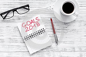 Set a goal for new year 2018. Notebook near pen, glasses and cup of coffee on grey wooden background top view