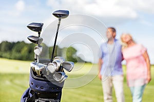 Set of golf clubs with senior couple in the background.