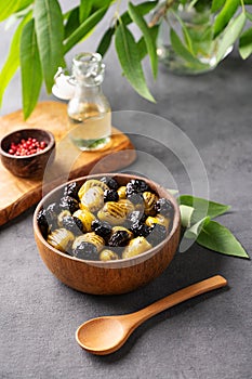 A set of green and black dried olives in bowl on a dark background with olive oil and eucalyptus branch. The concept of vegetarian