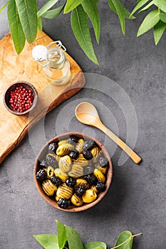 A set of green and black dried olives in bowl on a dark background with olive oil and eucalyptus branch. The concept of vegetarian