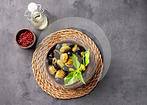 A set of green and black dried olives in bowl on a dark background with olive oil and red pepper. The concept of vegetarian