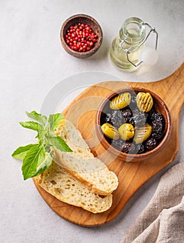 A set of green and black dried olives in bowl with fresh ciabatta slices on a light background with olive oil and basil close up