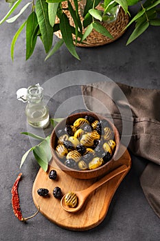 A set of green and black dried olives in bowl on a wooden cutting board on a dark background with olive oil and eucalyptus branch