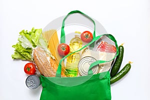 Set of grocery items from vegetables, canned food, pasta, oil, cereal in green eco shopping bag on white background. Top photo