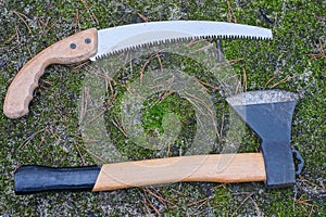 a set of hacksaw, lopper and ax lie on the ground and green moss