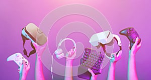 Set of hands with gamepad, keyboard, virtual reality headset and headphones on violet background.