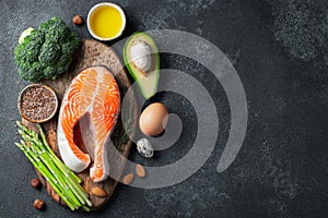 A set of healthy food for keto diet on a dark background. Fresh raw salmon steak with flax seeds, broccoli, avocado, chicken eggs