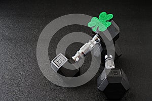 Set of hex head dumbbells with a green glitter shamrock on a black gym floor, happy St. Patrick’s Day