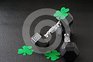 Set of hex head dumbbells with green glitter shamrocks on a black gym floor, happy St. Patrick’s Day