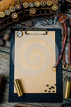 Set of hunting equipment on vintage desk. Hunting belt with cartridges, and clipboard with paper on wooden background