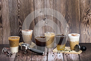 Set of iced coffee drinks arranging on dark brown wooden floor and background decorated by coffee beans group handle and tamper