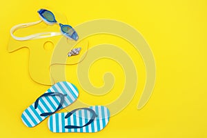 set of items for the beach - a toy, swimming goggles, children's flip flops on yellow background with copy space