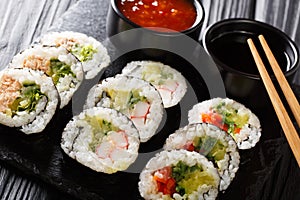 Set of japanese rolls futomaki with soy and chili sauces close-up on a slate board. horizontal