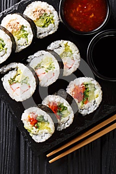 Set of japanese rolls futomaki with soy and chili sauces close-up on a slate board. Vertical top view