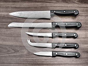 Set of kitchen knives on wood work surface. Filtered image.