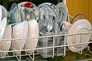 set of kitchen utensils made of white plates and metal spoons and forks in a dishwasher drawer