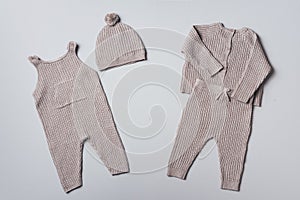 Set of knitted baby clothes. Newborn beige romper, hat, jumper, pants on neutral background. Winter, autumn unisex