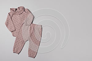 Set of knitted baby clothes. Newborn pink romper, pants, toys on neutral backgroundd. Winter, autumn unisex collection