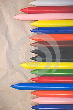 Set of lined up colored wax crayons on recycled paper background