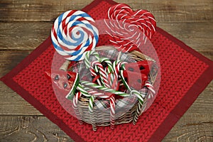 Set of lollipops in a basket in the form of a red heart, a candy cane, a watermelon and a ball on a wooden background.