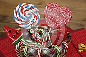 Set of lollipops in a basket in the form of a red heart, a candy cane, a watermelon and a ball on a wooden background.