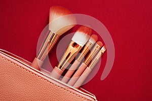 Set of make-up brushes and makeup products spilling out from pink cosmetics bag on to a red background. Top view.