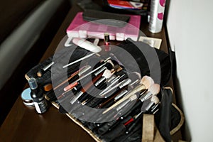 A set of makeup brushes in an open black cosmetic bag on a wooden table with cosmetics. Makeup artist set.