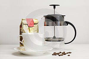 Set for making coffee at home - a French press, a bag of ground coffee and a porcelain cup