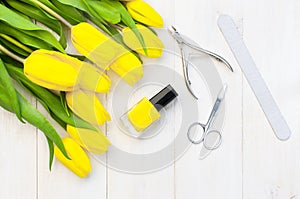 Set for manicure or pedicure, bright nail polish, scissors, nippers, tongs and nailfile with yellow tulips on a light photo