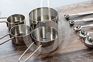 Set of measuring cups and measuring spoon with a handle made from stainless on wooden tabletop in eye level shot.