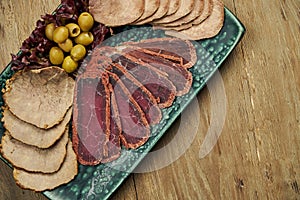 Set of meat antipasti - sliced baked tongue, ham, boiled pork and basturma on a blue plate on a wooden background. Beer snack