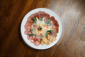 Set of meat antipasti - sliced salami, ham, boiled pork and basturma on a white plate on a wooden background. Beer snack